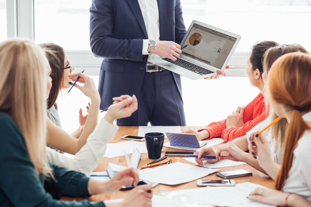 Ejecutivo con un portátil habla para un grupo de mujeres en una reunión